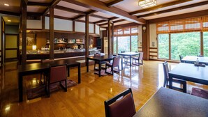 Un restaurant avec des poutres en bois, un coin bar et de grandes fenêtres donnant sur un paysage verdoyant.