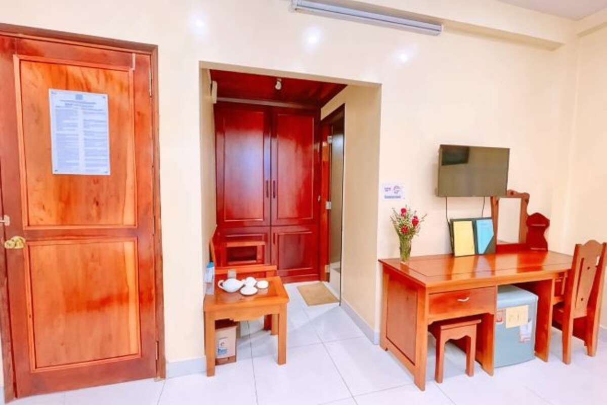 Una habitación con puerta de madera, un escritorio con silla, un televisor y una pequeña mesa con tetera.
