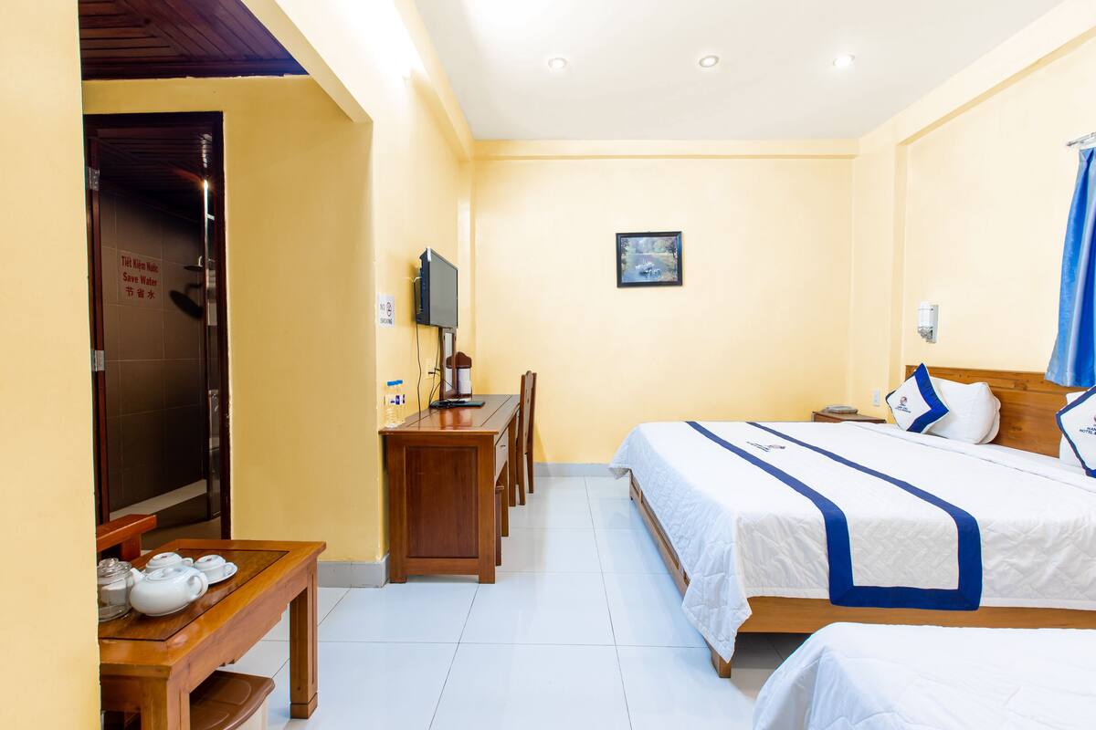 A hotel room with two beds, a desk with a TV, and a small table with teapots.