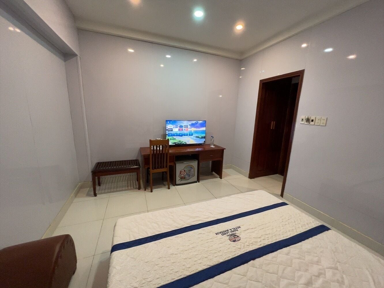 Una habitación de hotel con una cama, un escritorio con televisor, una silla y una mesita.