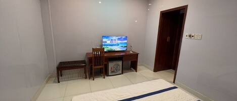 Una habitación de hotel con una cama, un escritorio con televisor, una silla y una mesita.