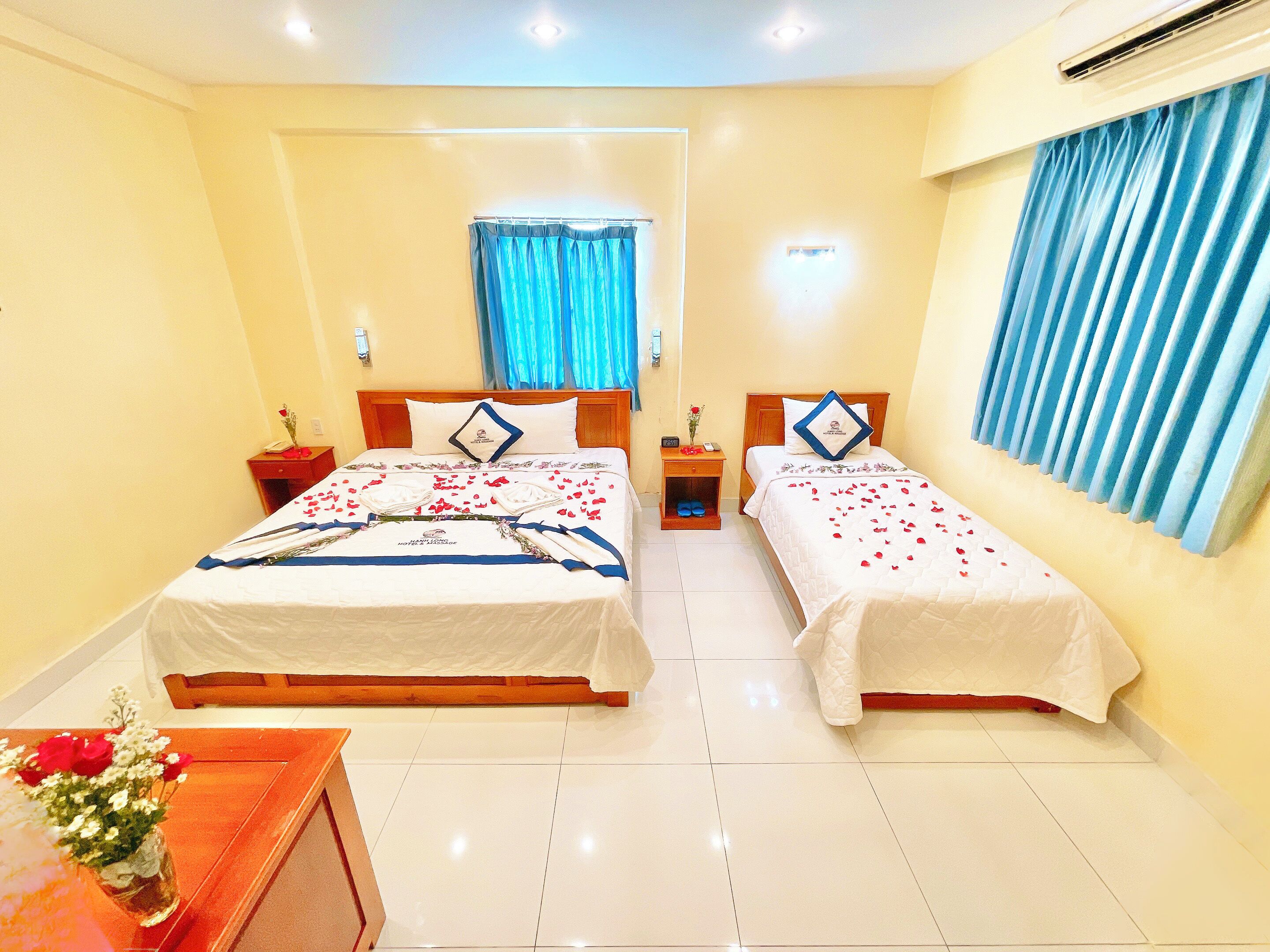 A hotel room with two beds, a nightstand, a desk, and a window with curtains.