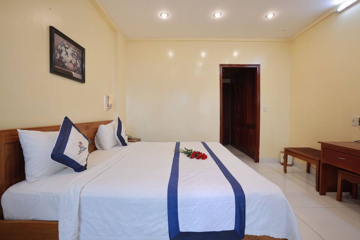 A hotel room with a large bed, a wooden headboard, a desk, and a door.