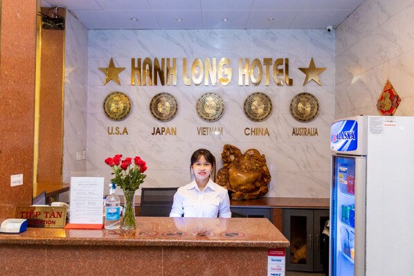 A hotel reception desk with a sign reading "HANH LONG HOTEL" and flags representing the USA, Japan, Vietnam, China, and Australia. - Hanh Long 1 Hotel (Ho Chi Minh City)