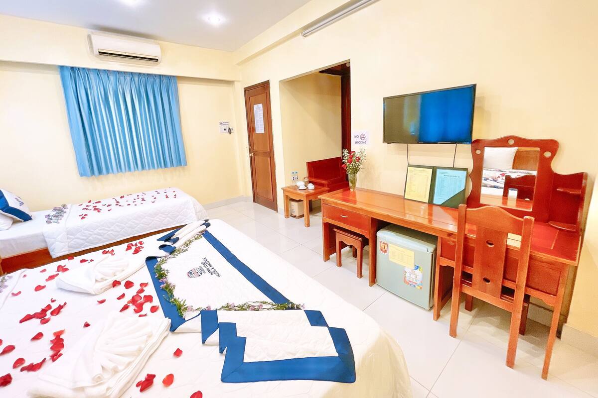 A hotel room with a bed, a desk, a chair, a television, and an air conditioning unit.