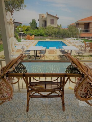 A poolside area with lounge chairs and tables, a clear view of the pool, and a building in the background.