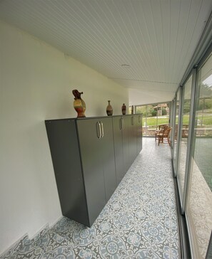 A long, narrow room with a patterned floor, a dark-colored cabinet with handles, and a glass door leading outside.