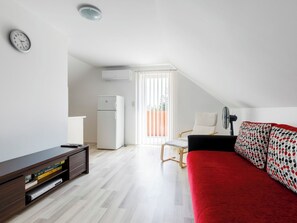Ett modernt, väl upplyst rum med ett trägolv, en röd soffa, en vit stol, ett litet bord och en klocka på väggen.