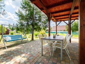Une terrasse couverte avec une table et des chaises, une balançoire et un banc.
