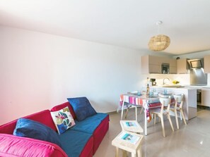 Un soggiorno moderno con un divano rosso e blu, un piccolo tavolino e una zona cucina con un piano di lavoro bianco ed elettrodomestici in acciaio inossidabile.