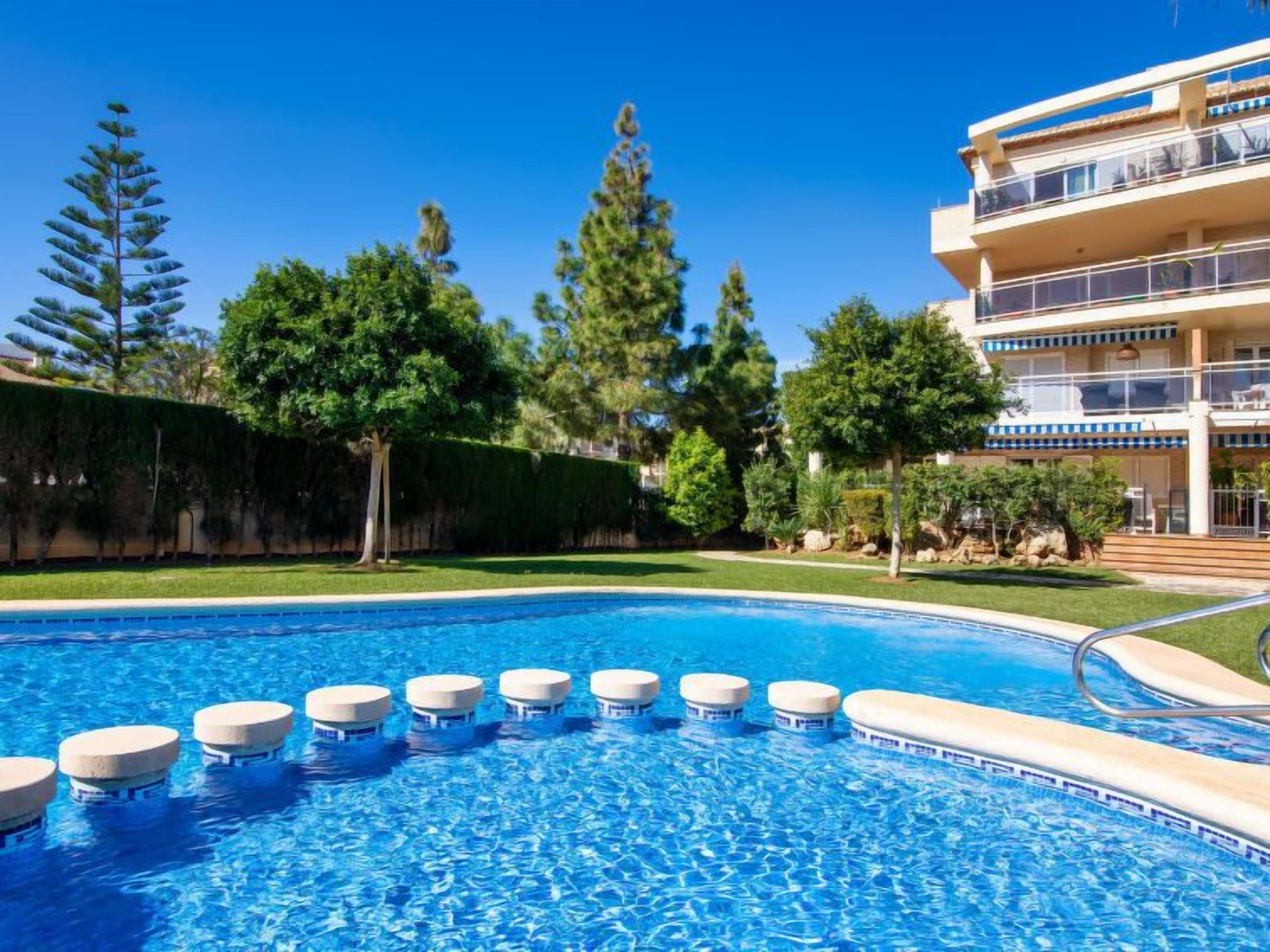 Une piscine dotée de plusieurs plateformes de plongeon, entourée d’une pelouse bien entretenue et d’arbres.