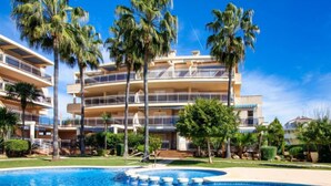 A multi-story hotel with a swimming pool surrounded by palm trees and a well-maintained lawn. - Los Aticos by Interhome (Dénia)