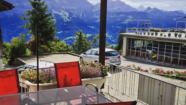 A balcony with a mountain view, a car parked nearby, and potted plants. - Lilo/Studio by Interhome (Beatenberg)