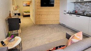 A modern living room with a grey sofa, a wooden entertainment unit, and a kitchen area with white cabinets and a stone backsplash. - Lilo/Studio by Interhome (Beatenberg)