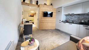 A modern kitchen with white cabinets, a stone backsplash, and a flat-screen TV mounted on a wooden wall. - Lilo/Studio by Interhome (Beatenberg)