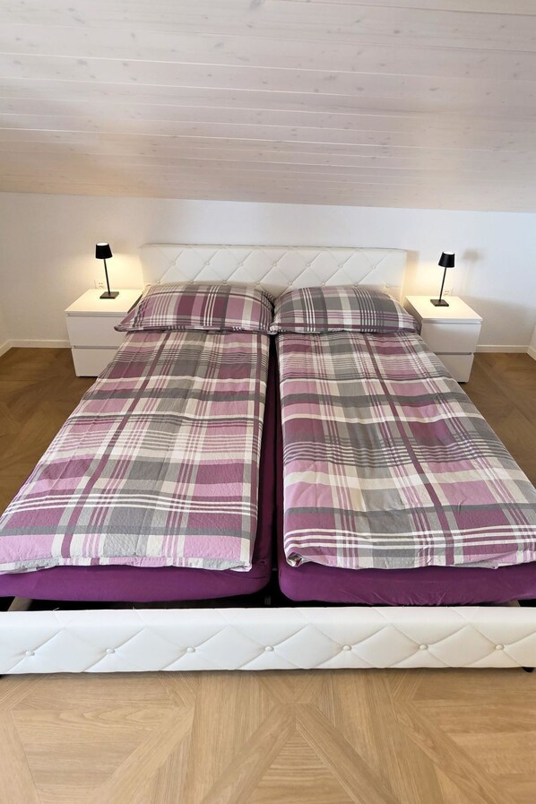 A twin bed with a plaid bedspread, two bedside tables with lamps, and a wooden floor.