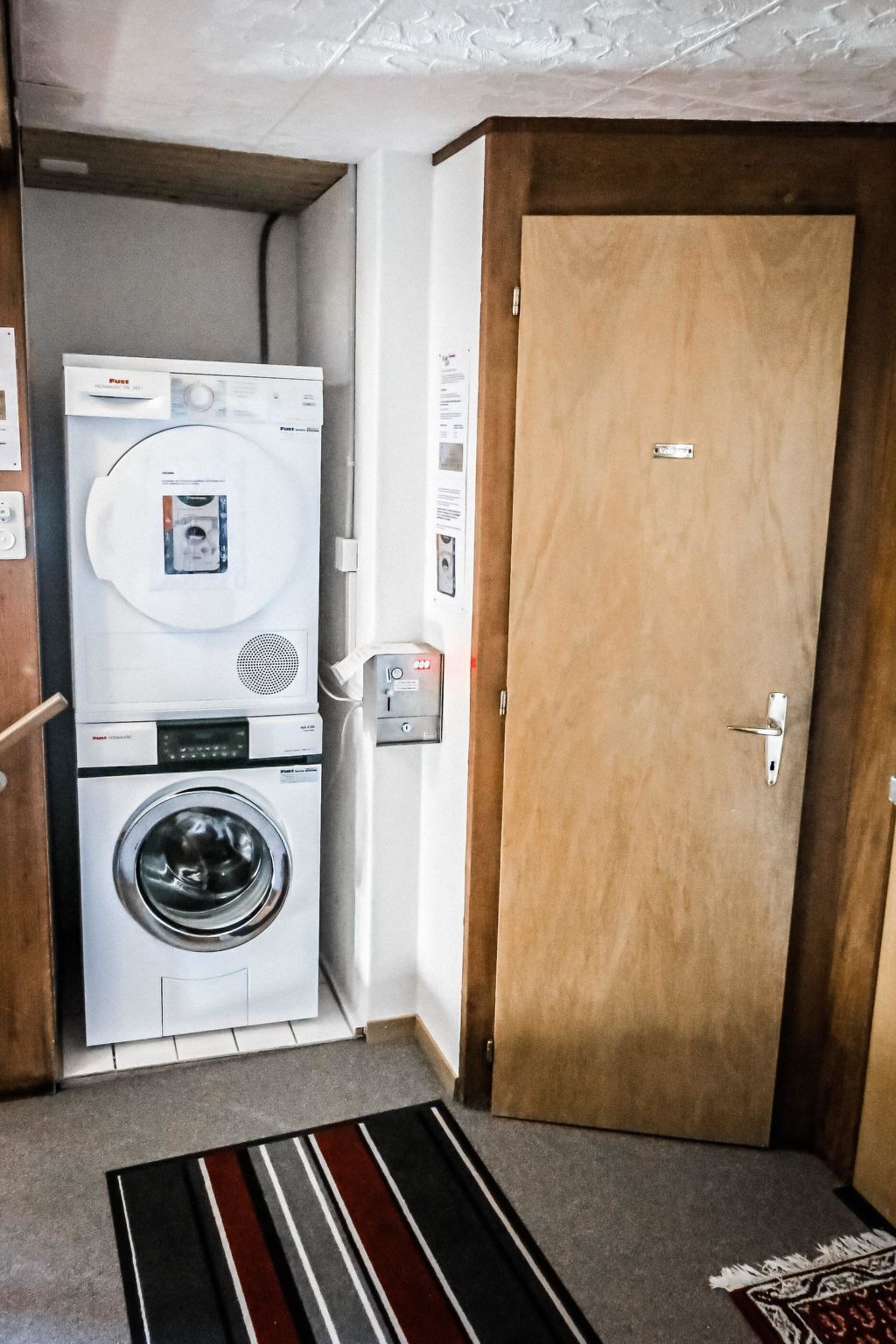 A laundry room with a washing machine and dryer, a wooden door, and a carpeted floor.