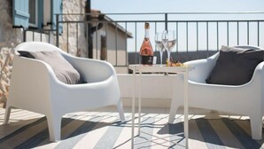A balcony with two white chairs, a small table with a bottle and glasses, and a stone building in the background. - Villa Caterina by Interhome (Novigrad (Istra))