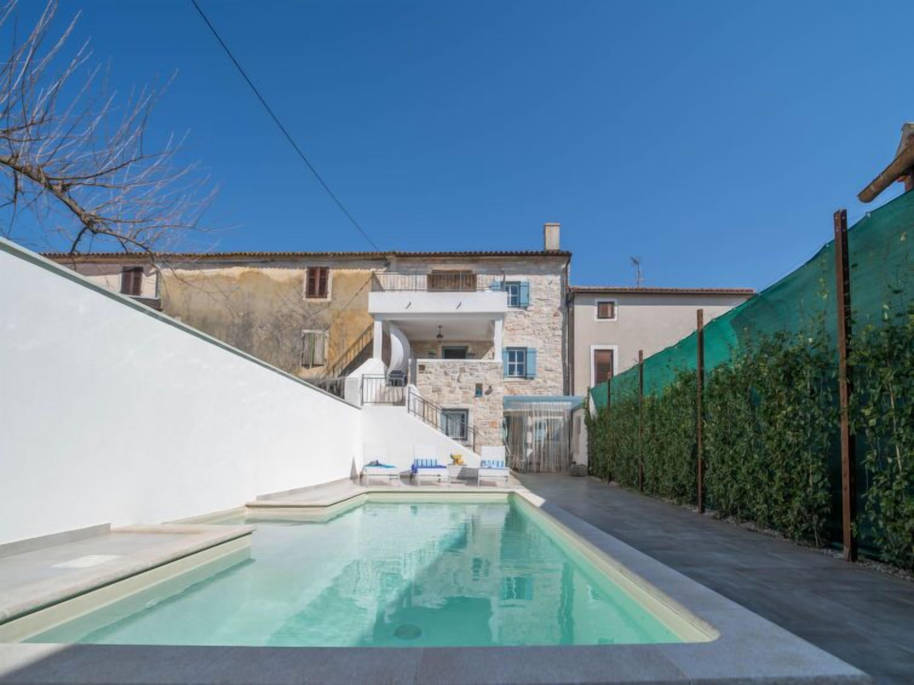 En bostadsfastighet med en swimmingpool, väggar av sten och puts, samt ett grönt staket.