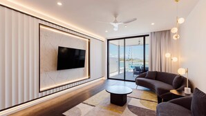 A modern living room with a flat-screen TV, dark sofas, a round coffee table, and a large window offering a view of the sea. - NEW! Dacha #2. First Class Luxury Waterfront Villa (Nelly Bay)