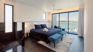 Une chambre moderne avec un grand lit, un banc, une vue sur la mer et un balcon.