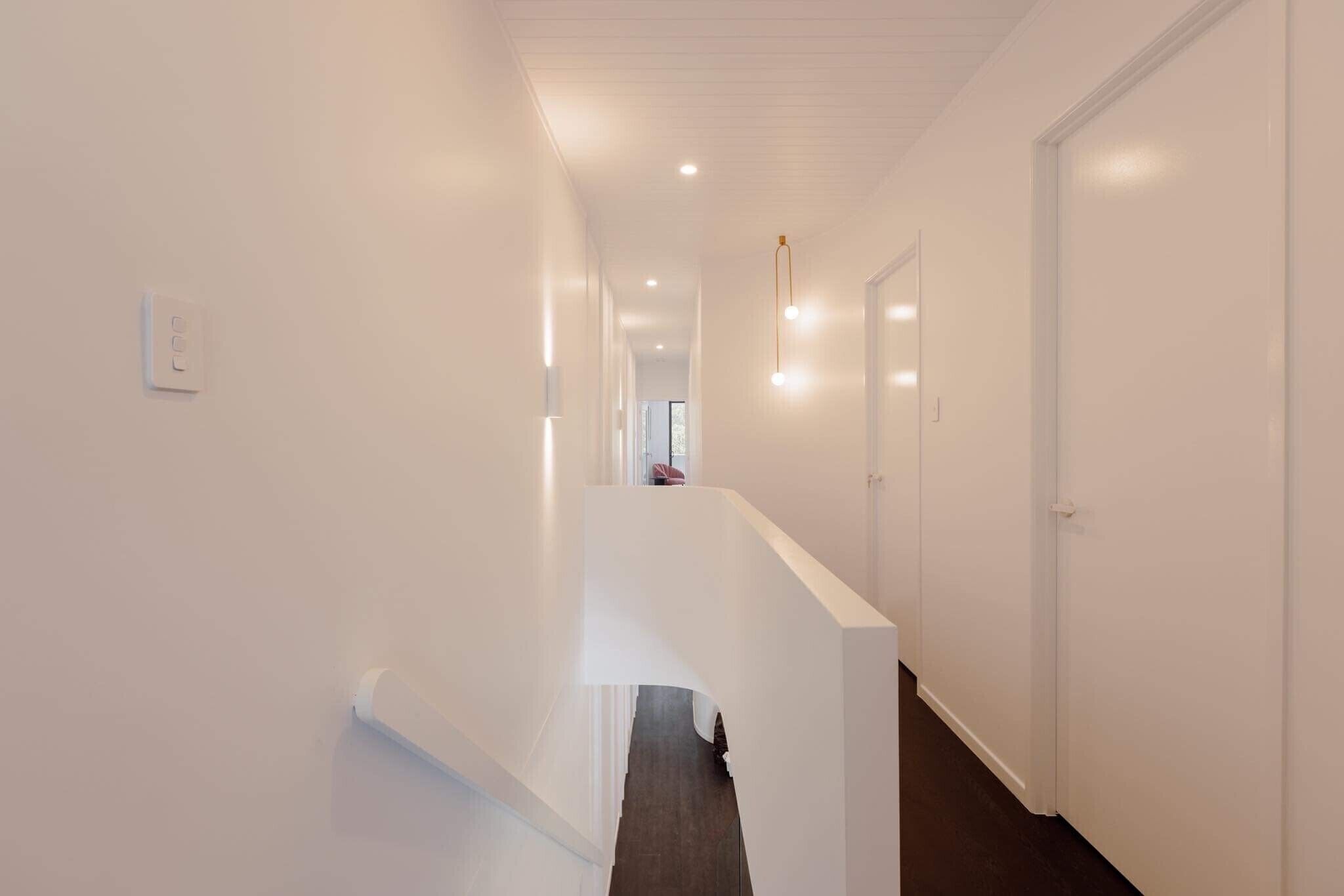 A modern, well-lit hallway with white walls and a dark floor, leading to a door at the end.