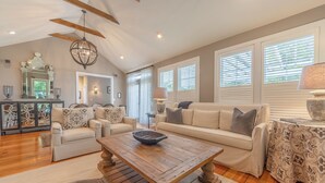 A spacious living room with a wooden coffee table, beige sofas, and a large window with blinds.