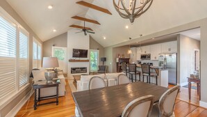 A spacious living room with a dark wooden dining table, white sofas, and a ceiling fan.