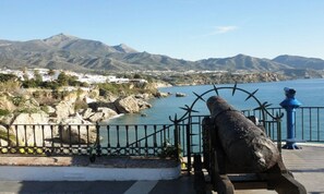 A coastal view with a stone cannon, a metal railing, and a clear sky.