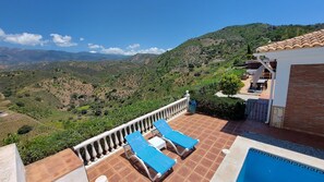 A terrace with two blue sun loungers, a small table, and a pool.