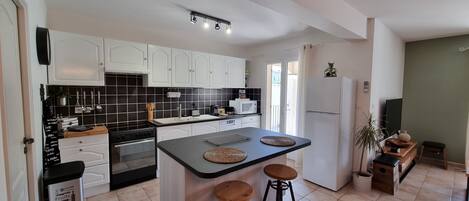 Una cocina moderna con armarios blancos, un salpicadero de azulejos negros, una isla central con taburetes y un refrigerador.