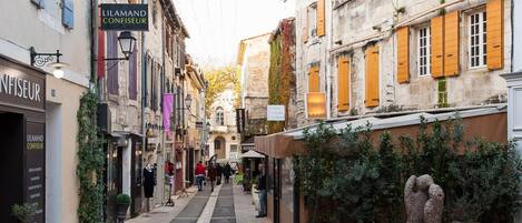 A narrow street lined with historic buildings, a café named 'LILAMAND CONFISEUR', and a statue in the foreground.