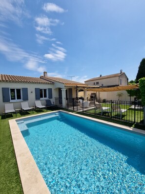 Une piscine rectangulaire avec une terrasse carrelée, entourée d’une pelouse et d’une clôture noire.