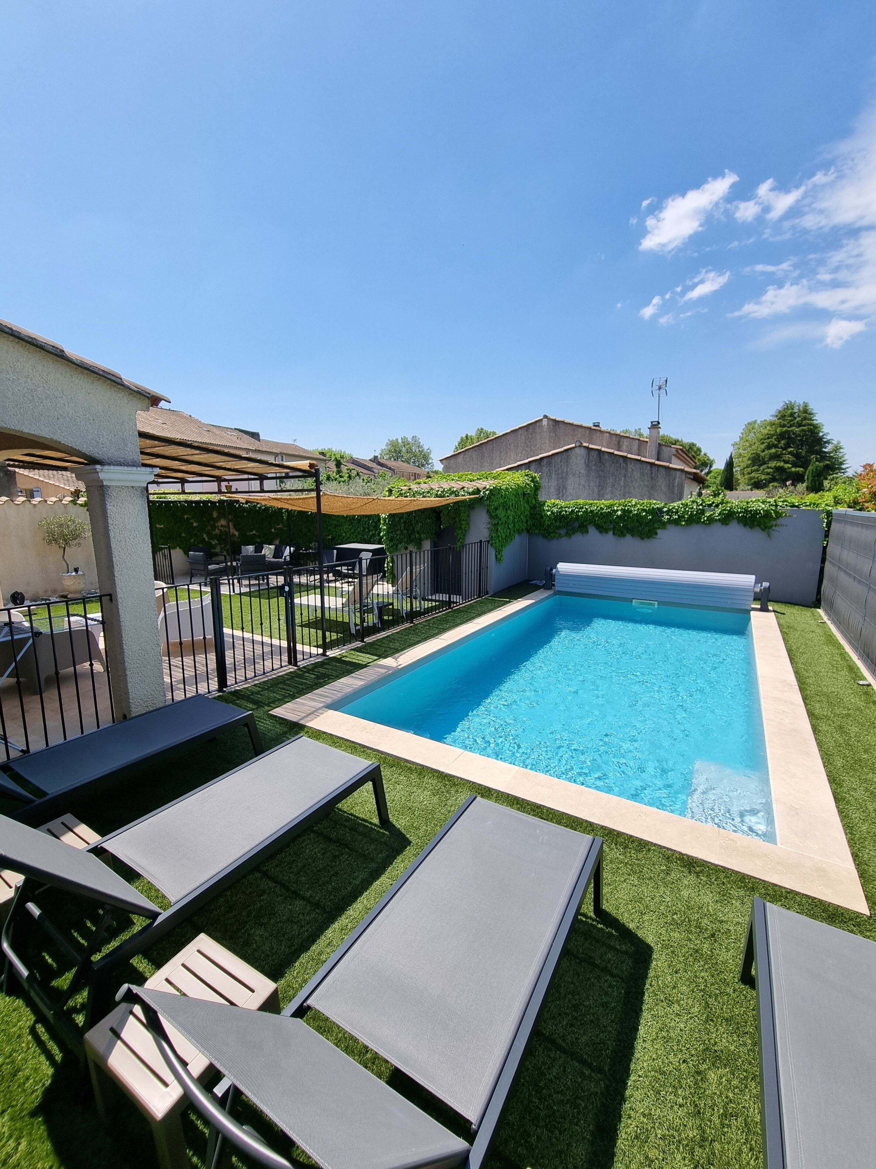 A rectangular swimming pool with a tiled edge, surrounded by artificial grass and black lounge chairs.