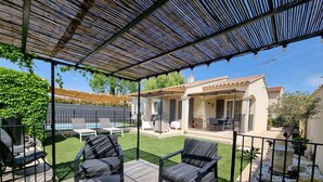 A covered patio with outdoor furniture, a pool, and a house in the background.