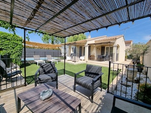 Une terrasse couverte avec des meubles d’extérieur, une piscine et une maison en arrière-plan.
