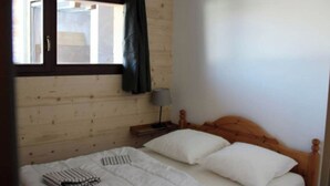 A single bed with white bedding and two pillows, a bedside table with a lamp, and a window with a curtain. - No. 2, capacity: 14 people (Vars)