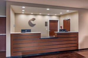 A reception desk with a wooden finish, a large C-shaped logo on the wall, and a door with a red fire extinguisher.