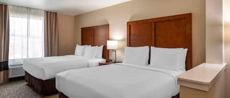 Habitación de hotel con dos camas, una mesita de noche con lámpara, una ventana con cortinas y piso alfombrado.