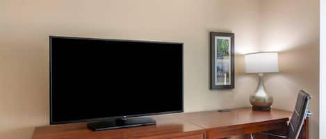 Hotelkamer met flatscreen televisie, bureau met lamp, stoel en een ingelijste foto aan de muur.