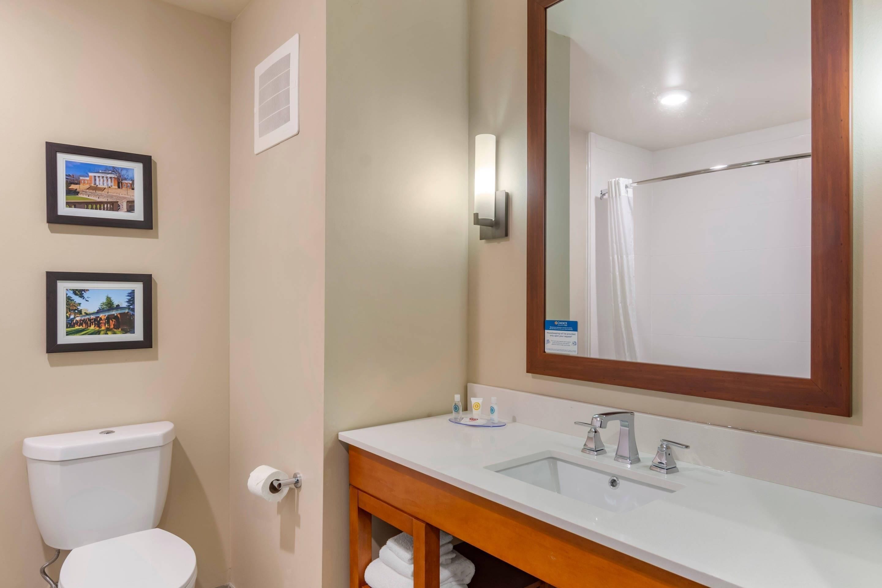Une salle de bain avec des toilettes, un lavabo et un miroir. Des tableaux encadrés ornent le mur.
