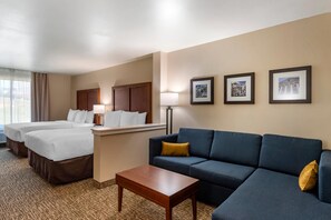 A hotel room with two beds, a sofa, a coffee table, and framed pictures on the wall.