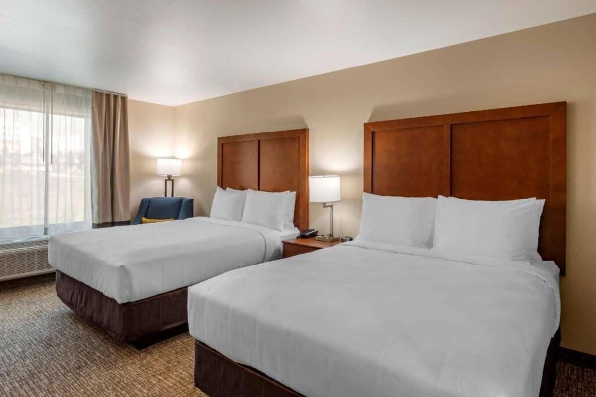 A hotel room with two beds, a desk, a chair, and a window with curtains.