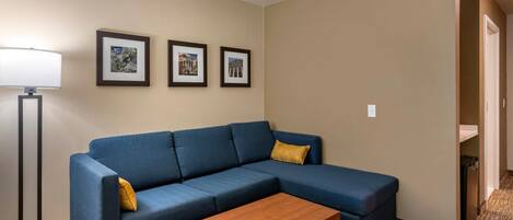 Una habitación con un sofá azul, una mesa de centro de madera y tres cuadros en la pared.
