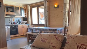 Ett mysigt rum med en säng i trä, ett matbord och en köksdel med träskåp och en spis.