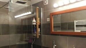 Ett modernt badrum med en dusch som är avskärmad med glasväggar, en stor spegel och en vit handfat.
