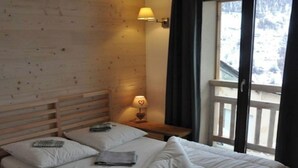 A wooden room with a bed, a nightstand, a lamp, and a window with a view of snow. - No. 6, maximum 14 people (Vars)