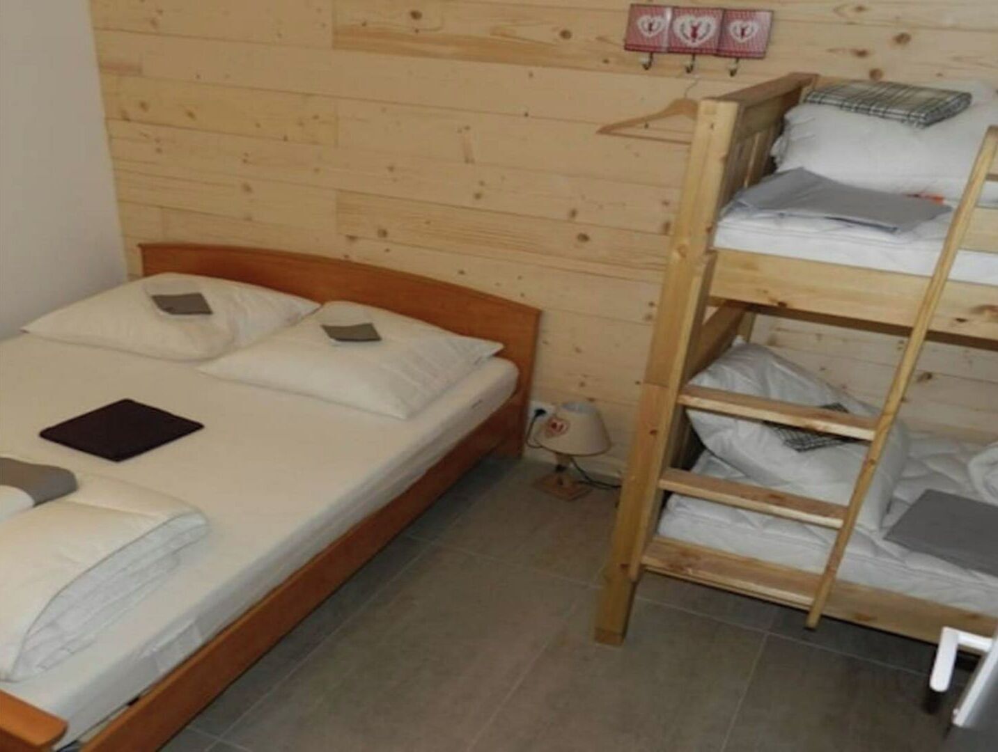A wooden bunk bed room with a single bed and a bunk bed. There is a small table and a lamp near the bunk bed.