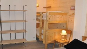 A room with a wooden bunk bed, a small wooden chair, a bedside table with a lamp, and a metal shelf unit against the wall. - No. 6, maximum 14 people (Vars)