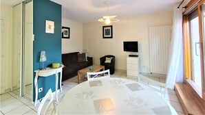 A compact living space with a blue accent wall, a round dining table, a sofa, a TV, and a window with curtains.